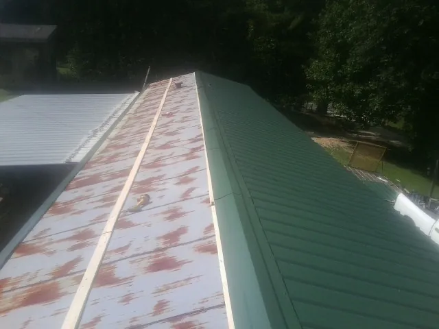 Old rusted panels beside newly installed green metal roofing — Wind Damage Roof Repair by Roofing Brothers in Port Saint Lucie