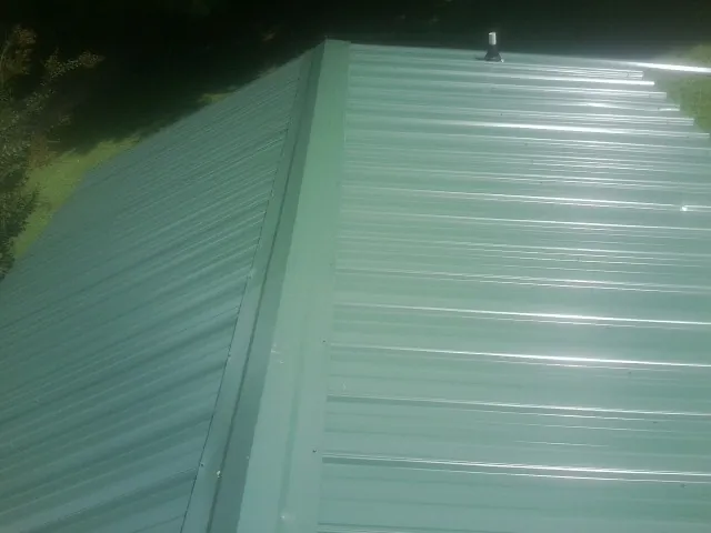 New green metal panels meeting at the ridge of a roof — Flat Roof Repair work by our crew in Port Saint Lucie