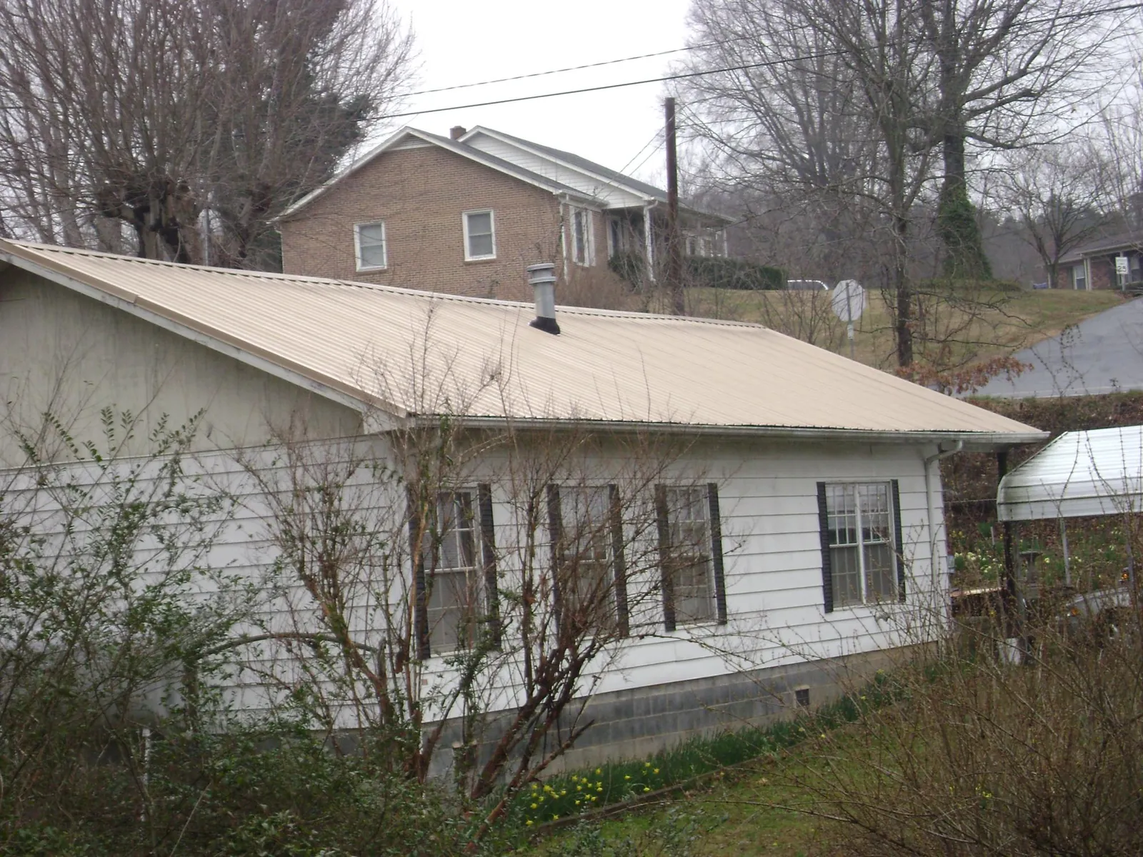 Tan metal roof on a white sided house set into a hillside — Commercial Roofing by Roofing Brothers in Port Saint Lucie