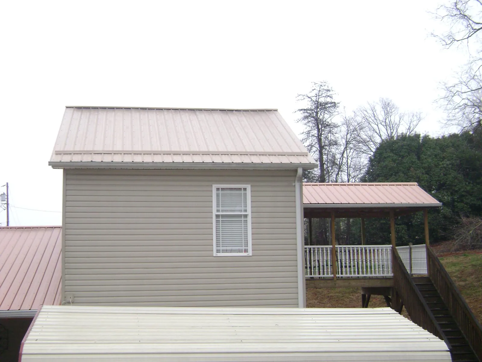 Tan metal roofs on a two story addition and attached porch, from a Roof Replacement job in Port Saint Lucie